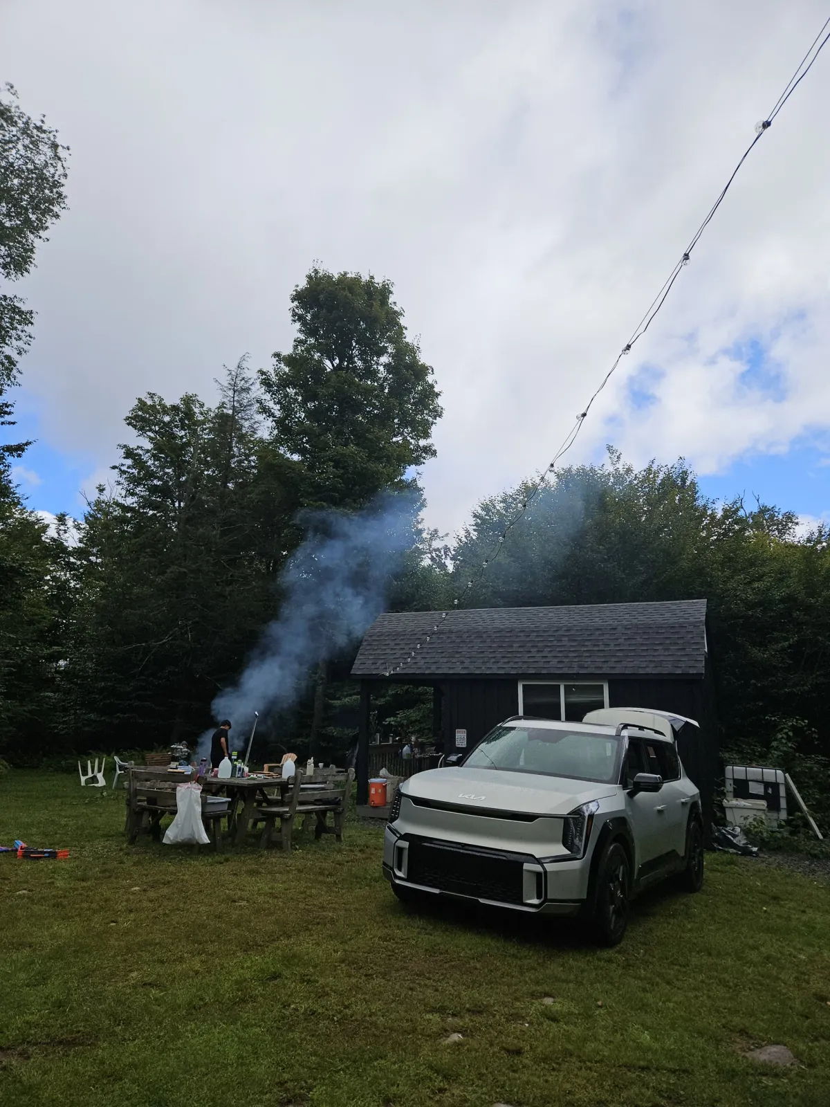 The Kia EV9 parked on grass at a Catskills campsite beside a picnic table and a smoking fire
