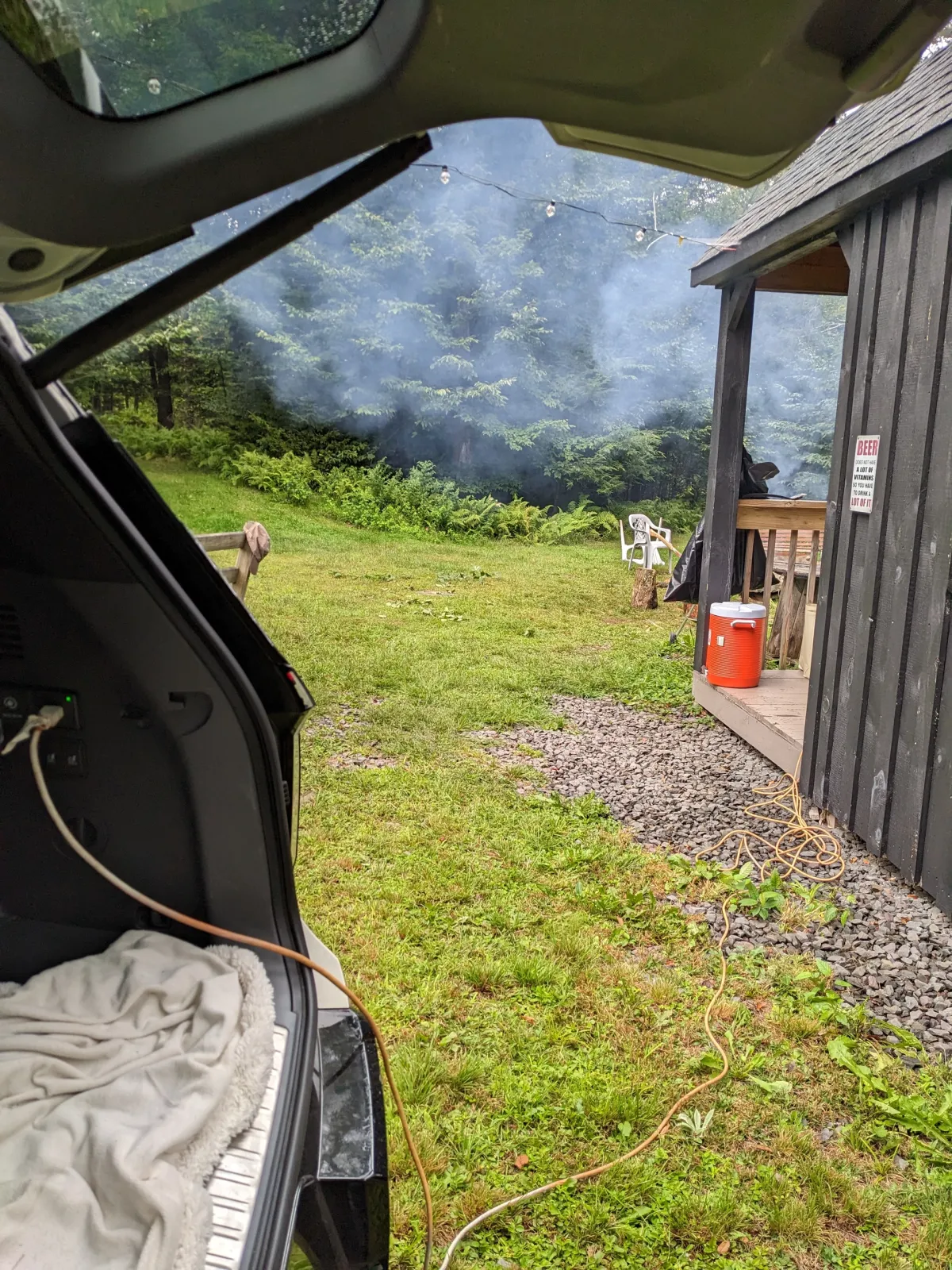 An extension cord running from the Kia EV9's cargo-area power outlet across the grass to a cabin